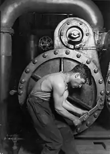 Image 21Lewis Hine's 1920 image "Power house mechanic working on steam pump," which shows a working class young American man with wrench in hand, hunched over, surrounded by the machinery that defines his work.